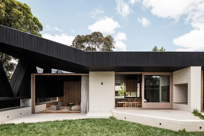Rear courtyard with white brick walls, timber-framed glazing and a cantilevered black timber roof under midday sun
