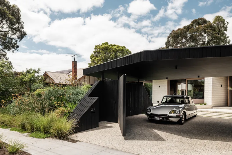Carport with angled black timber cladding and a vintage sedan parked beneath the sweeping roof overhang