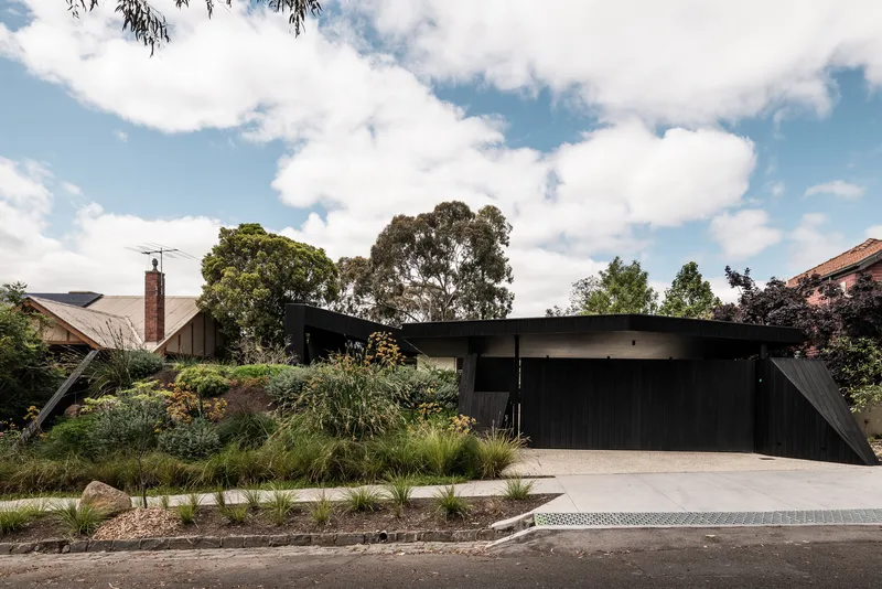 Street view of the black timber and concrete facade behind native grasses and gravel beds