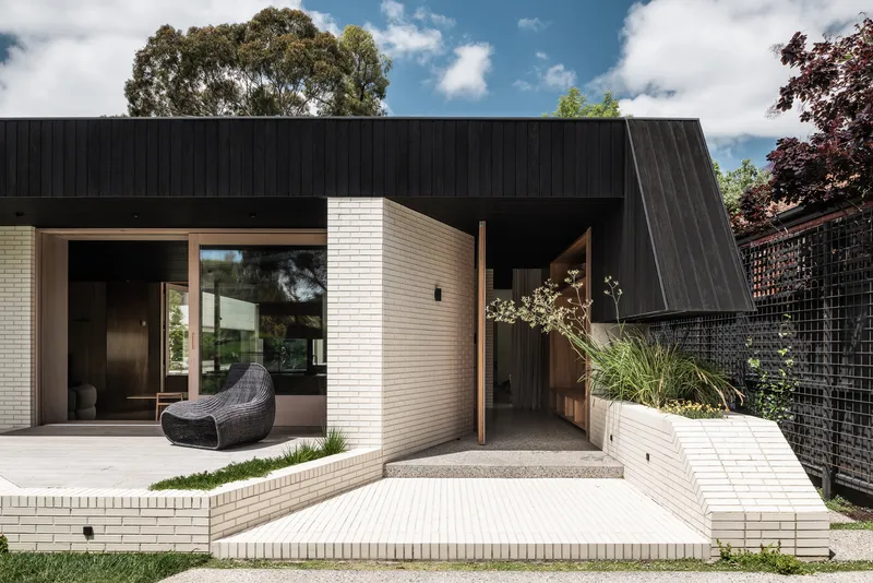 Courtyard view with cream brick walls, timber threshold, and angled black cladding against the planted boundary