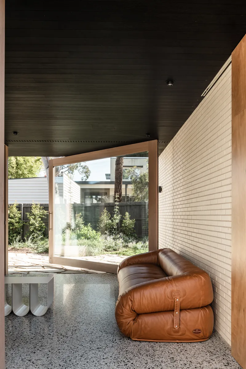 Covered entry nook with terrazzo floor, timber door frame and brown leather seating beneath black timber ceiling