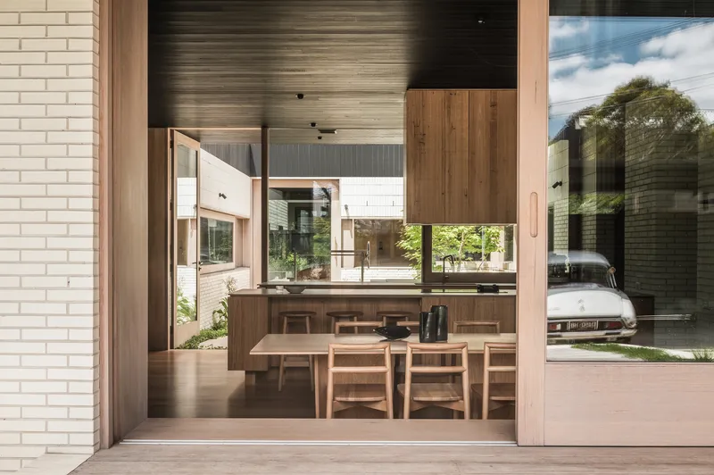 View through sliding doors to the dining area with timber table and chairs beneath a dark slatted ceiling
