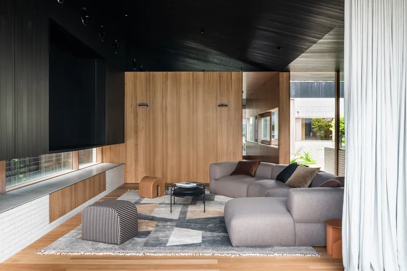 Living room with sectional sofa and timber storage wall beneath a dark timber slatted ceiling