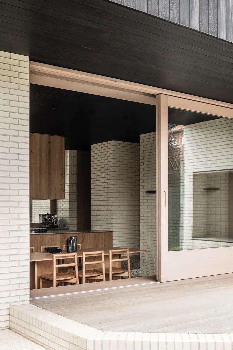 Framed opening with timber surround revealing dining area and white brick courtyard walls beyond