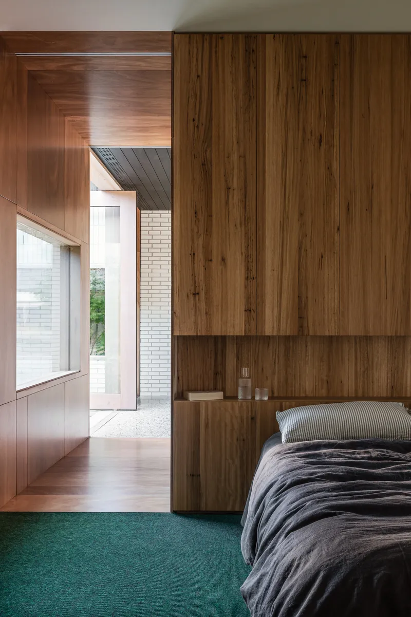 Bedroom with timber wardrobe wall and green carpet looking through doorway to exterior courtyard