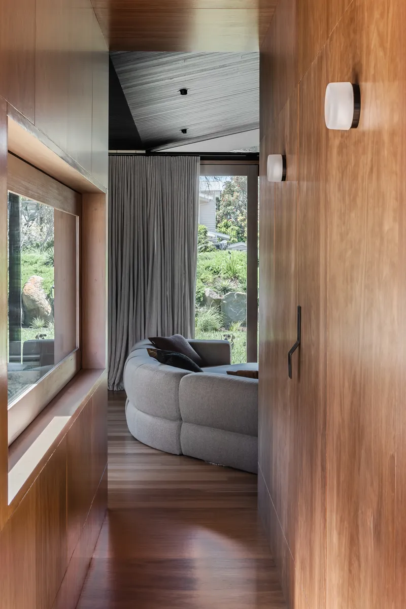 Hallway with timber walls and angled ceiling leading to living area with garden view