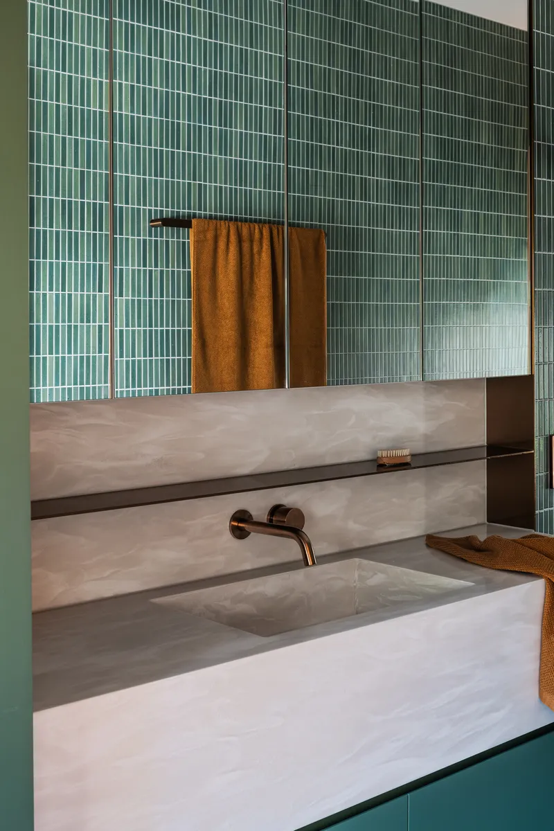 Bathroom vanity with integrated marble sink below green vertical tile and bronze wall-mounted tap