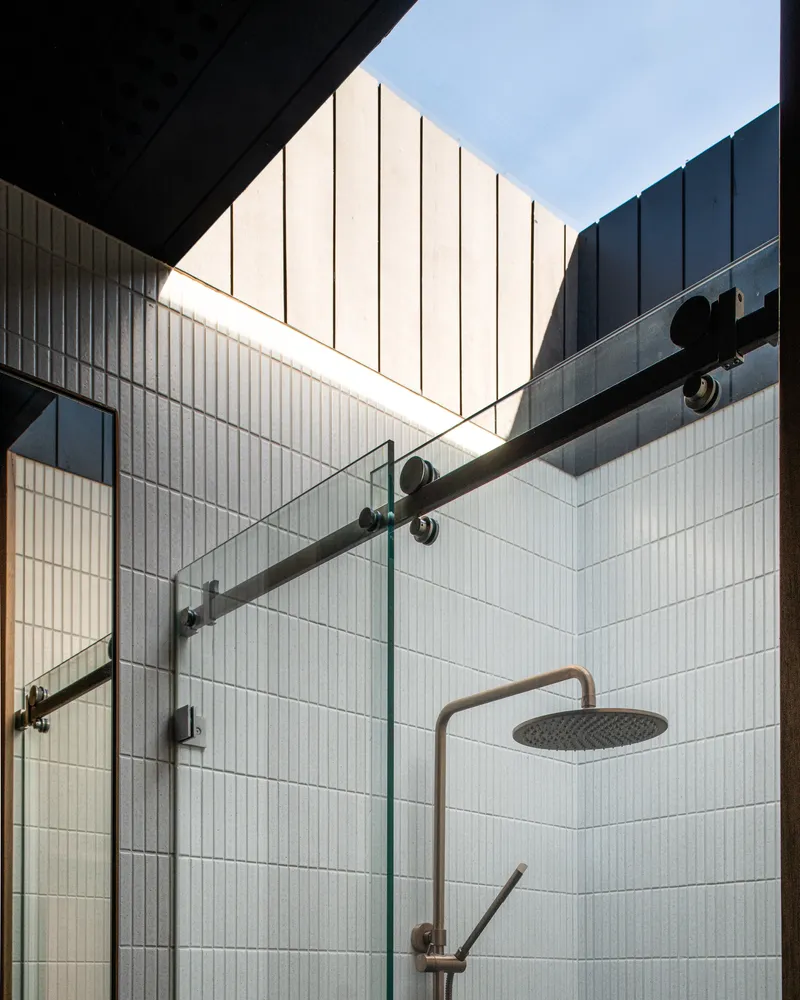 Open-air shower enclosure with glass partition and skylight above white vertical tile walls