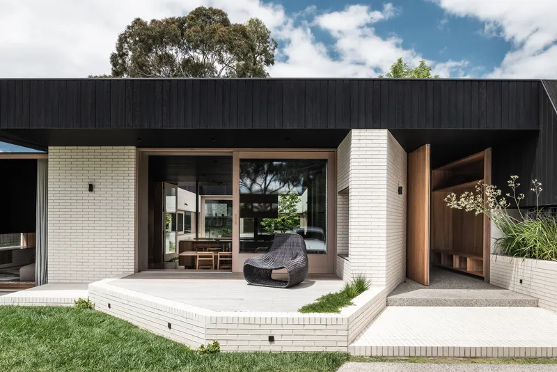 Raised concrete terrace with woven lounge chair facing glazed openings and cream brick planters