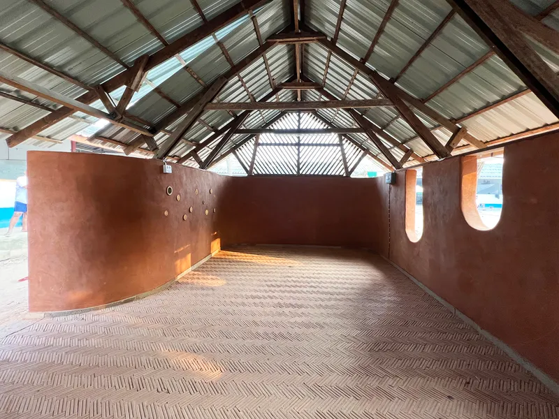 Interior of gabled space with exposed timber trusses, corrugated metal ceiling, and herringbone brick floor