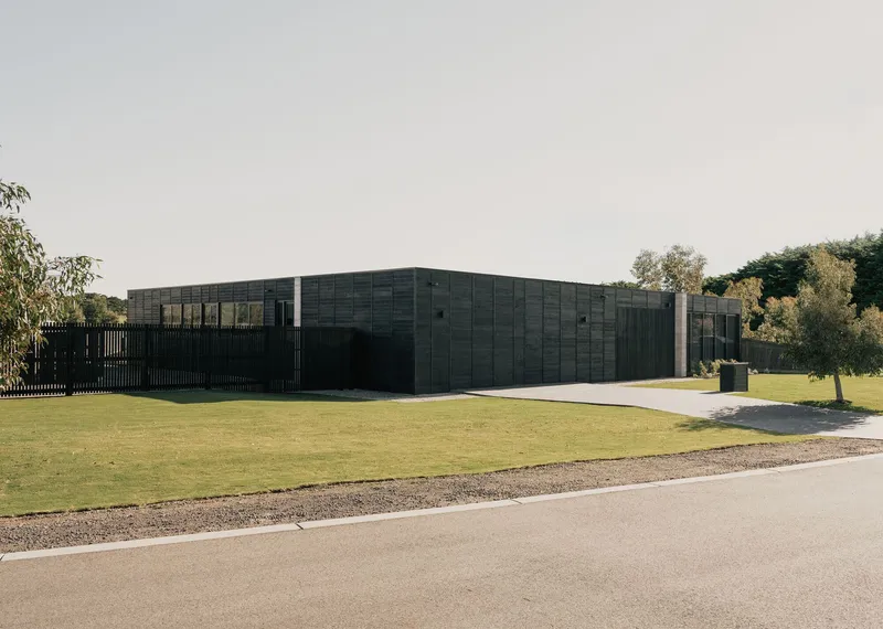 Corner view showing the charred timber cladding and vertical slat fence with trees in the background