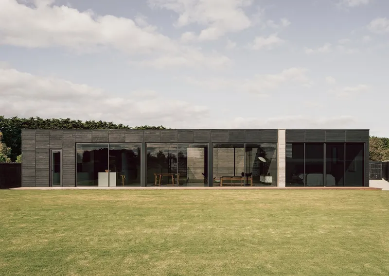 Garden facade with floor-to-ceiling glazing revealing interior furnishings under a cloudy sky