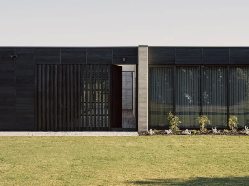 Close-up of the entry with vertical timber screen and concrete column against the dark cladding