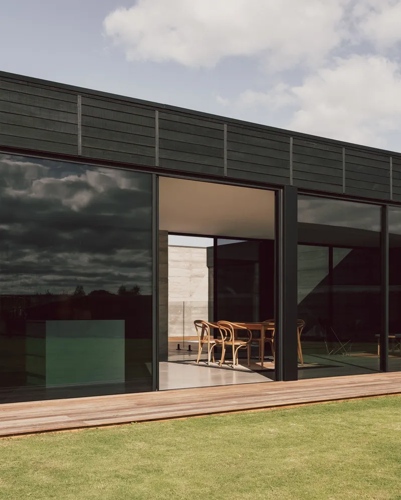 Timber deck and open sliding doors framing the dining table beneath darkening storm clouds