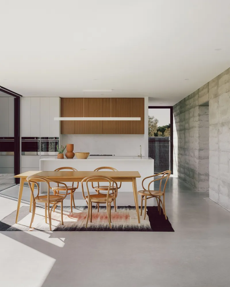 Open-plan dining space with board-formed concrete wall and afternoon sunlight on polished floor