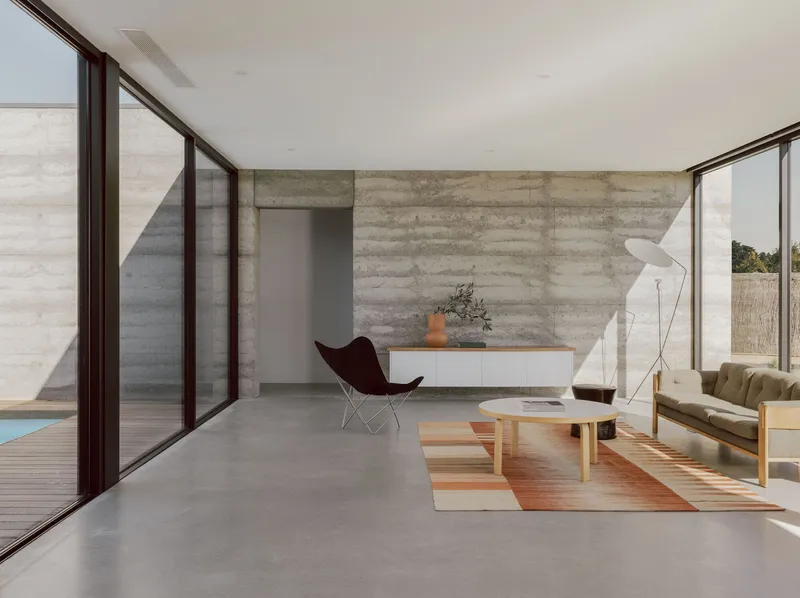 Living room with polished concrete floor and boardformed concrete wall catching diagonal afternoon light
