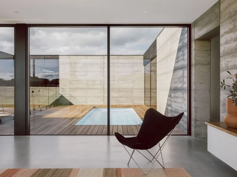 Glass-walled living space overlooking timber deck courtyard with pool and boardformed concrete walls beyond