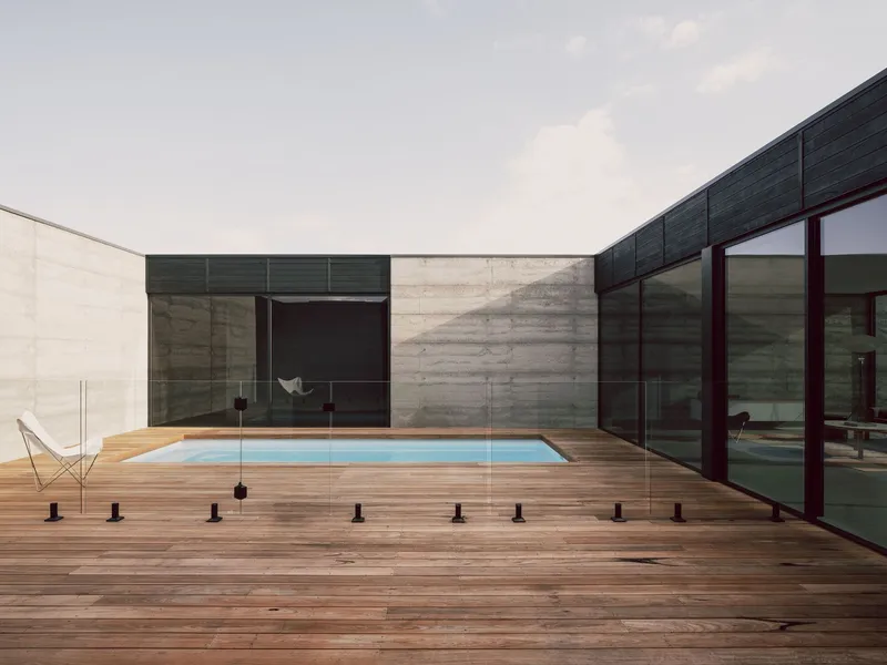 Timber deck courtyard with rectangular pool framed by boardmarked concrete walls and dark glazing