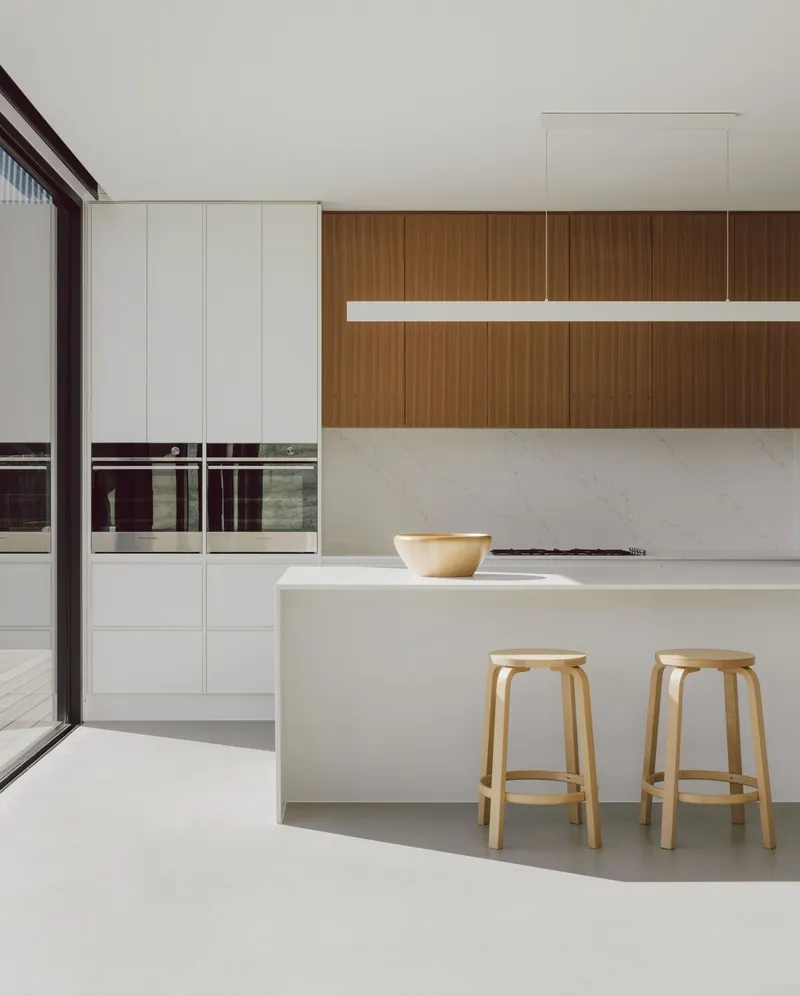 White island bench with timber stools beneath walnut cabinetry and linear pendant light fixture