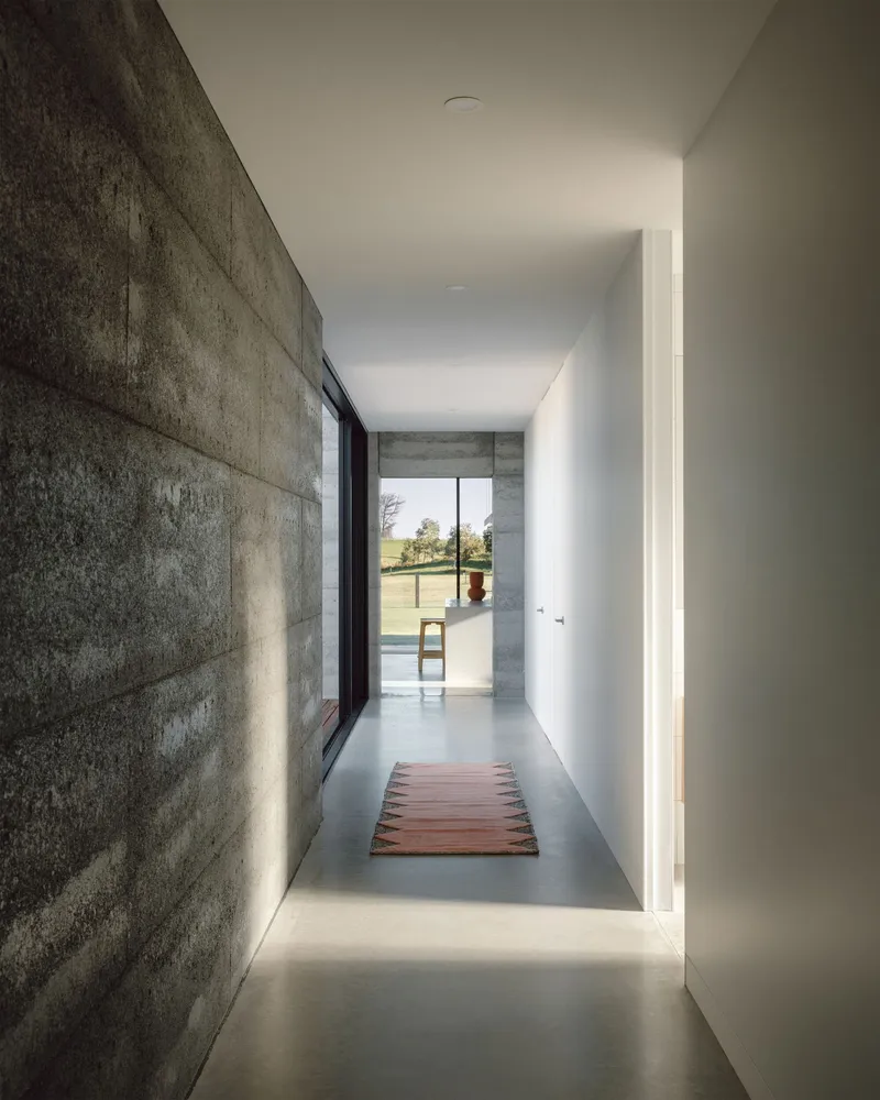 Concrete hallway with polished floor and cove lighting leading toward pool terrace in daylight