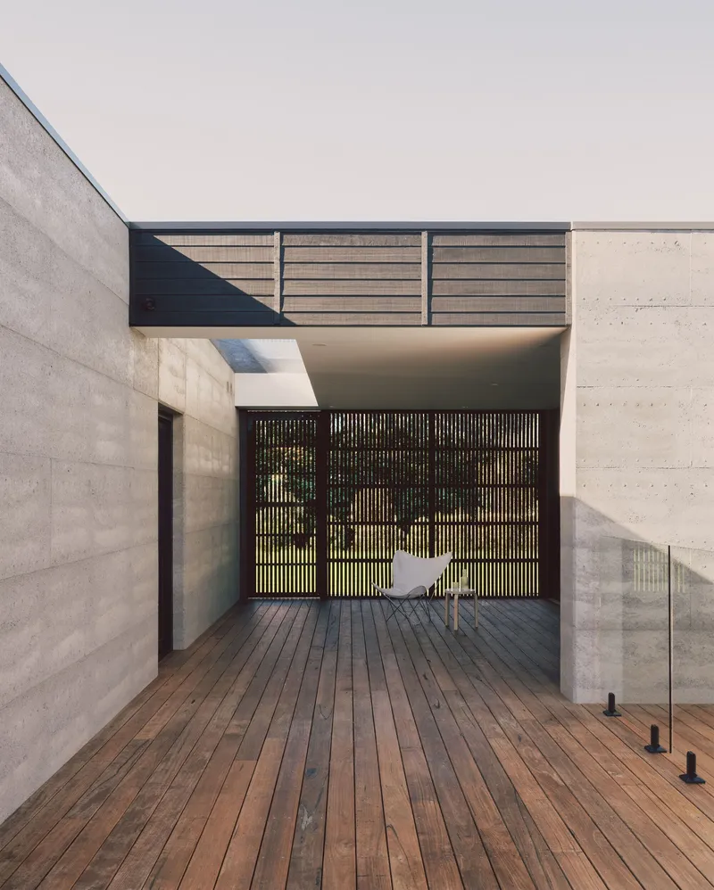 Covered timber deck entry with vertical slatted screen and white chair beneath concrete canopy