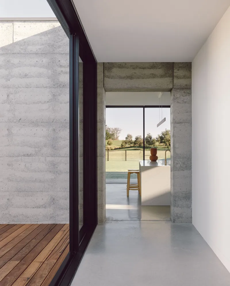 Concrete threshold opening from timber deck into interior with view toward distant landscape