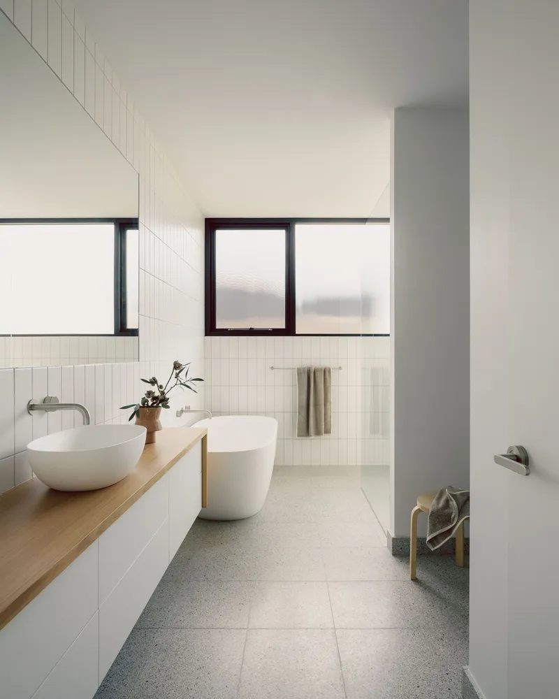 Bathroom with white vertical tile walls, timber vanity and freestanding tub beside terrazzo flooring