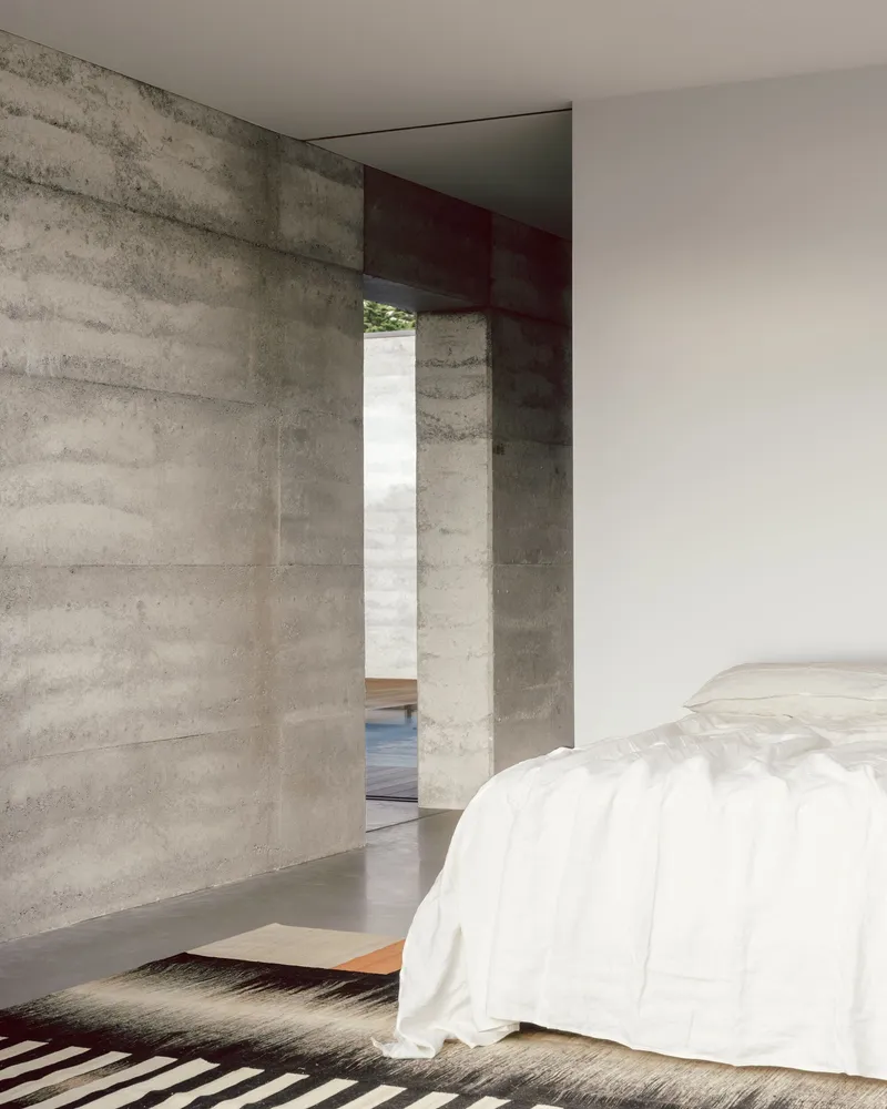 Bedroom with board-formed concrete walls and a deep red steel beam framing the doorway