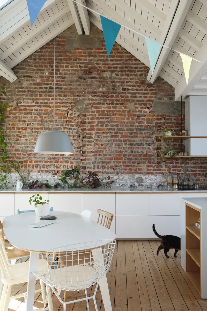 Kitchen dining area with exposed brick wall and painted timber rafter ceiling above a black cat