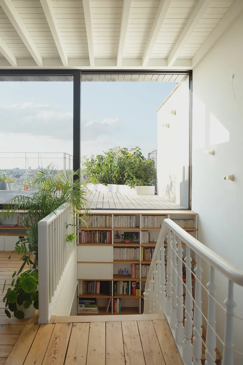 Landing with built-in bookshelf overlooking a timber deck terrace through a large glazed opening