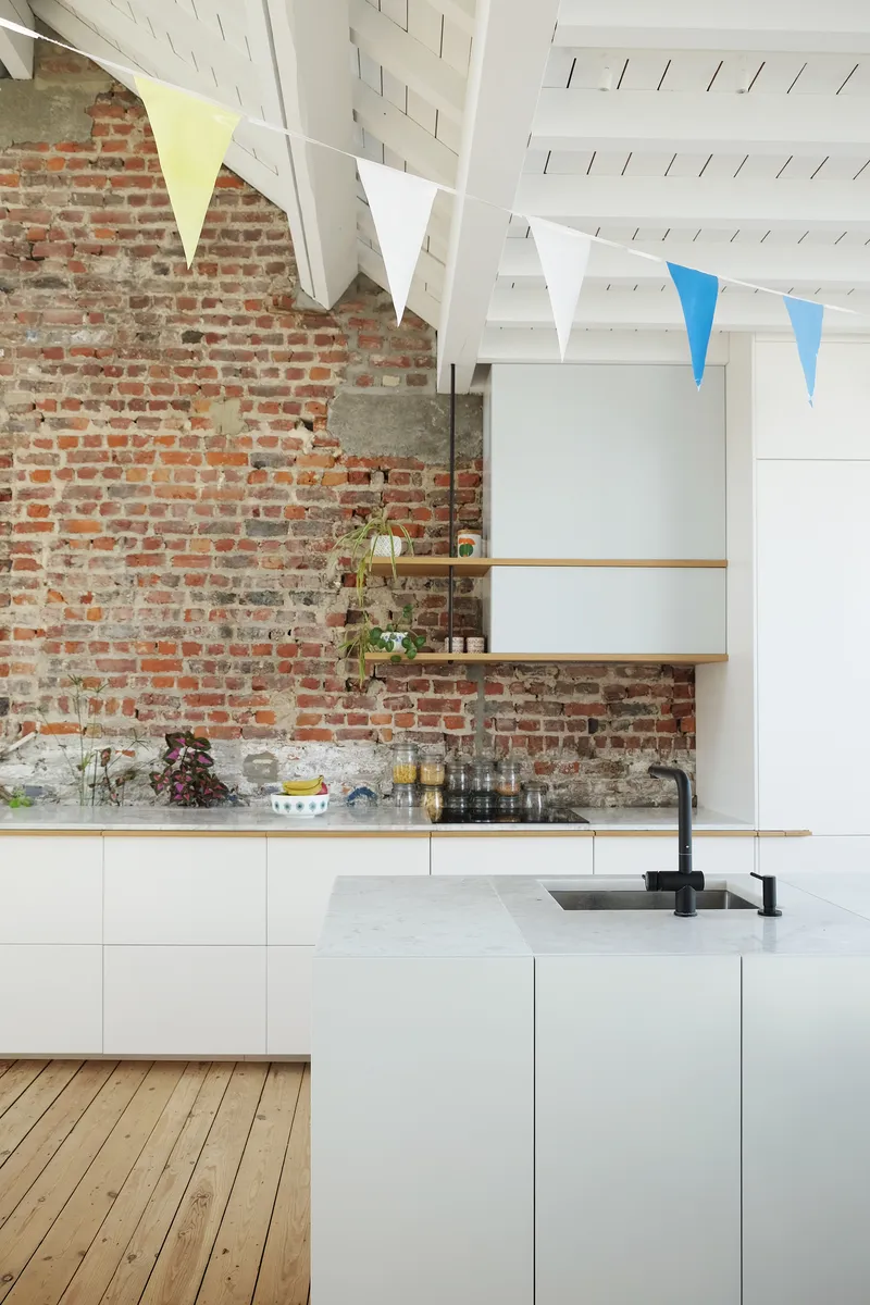 Kitchen with exposed red brick wall, white plank ceiling, and marble-topped island beneath colorful pennant flags