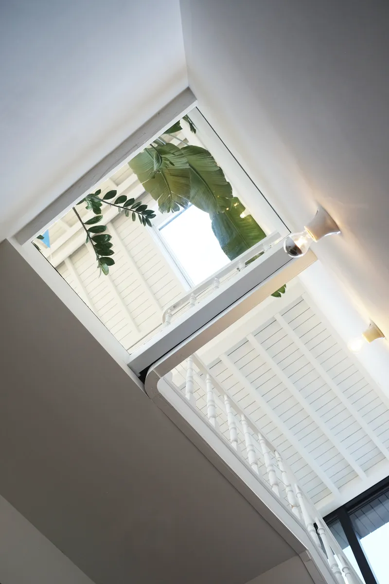 Upward view through the central atrium showing white-painted timber ceiling beams and foliage framing the opening