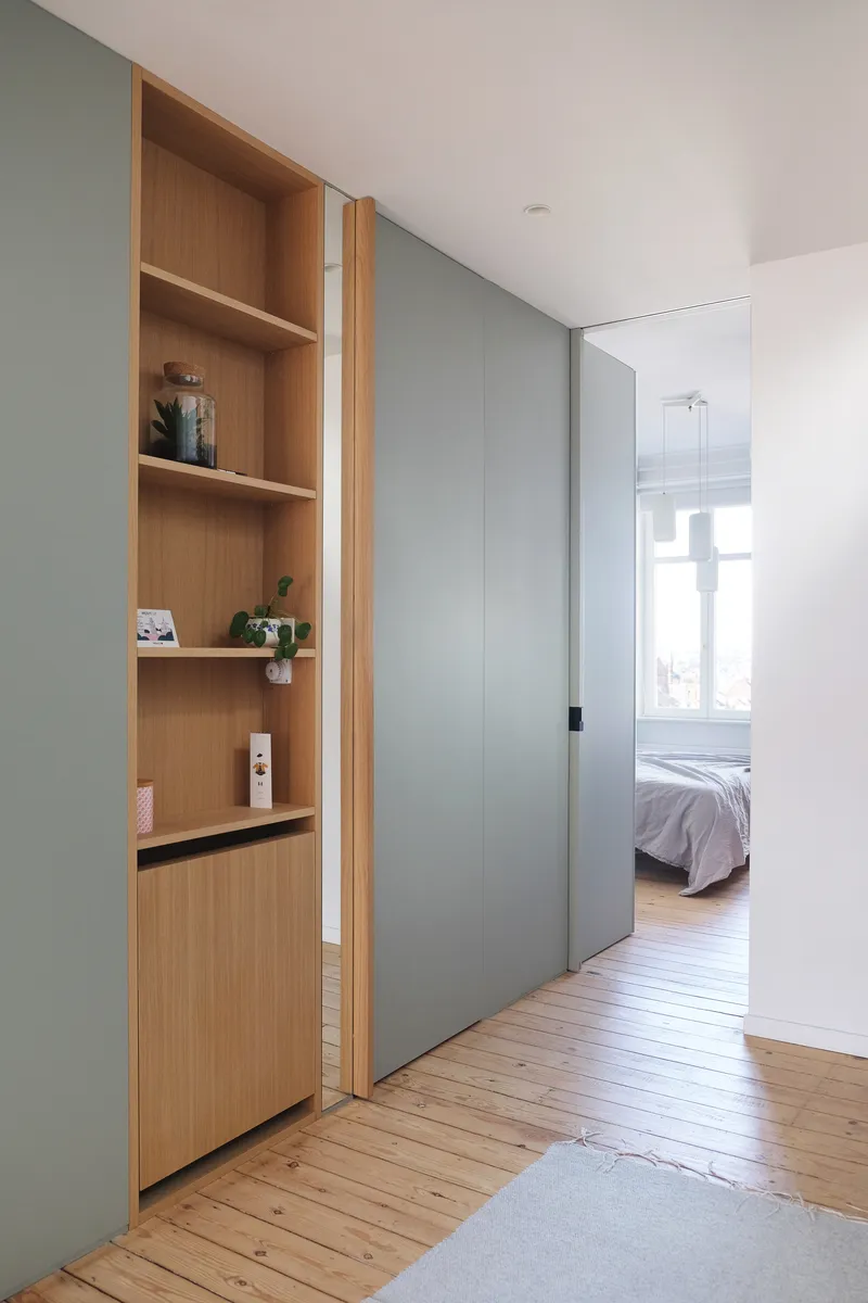 Corridor with grey sliding door, timber shelving niche, and view through to bedroom beyond on timber flooring