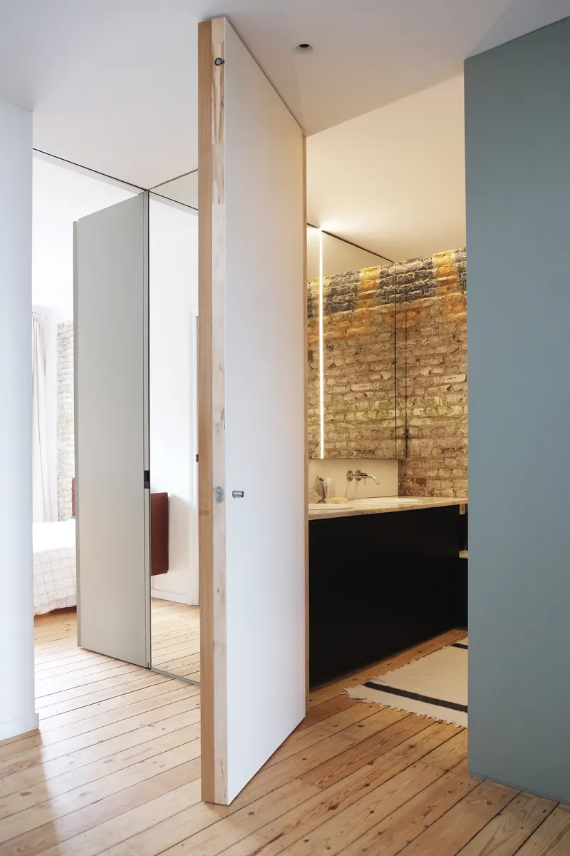 Bathroom entry showing black vanity against exposed brick wall lit by vertical strip lighting on timber floors