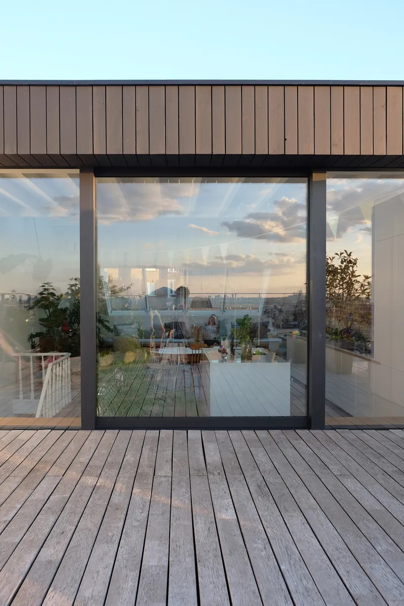 Timber-clad rooftop pavilion with floor-to-ceiling glass doors opening onto a deck at dusk