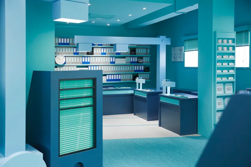 View through columns showing navy workstations with illuminated panels against turquoise walls and blue carpet