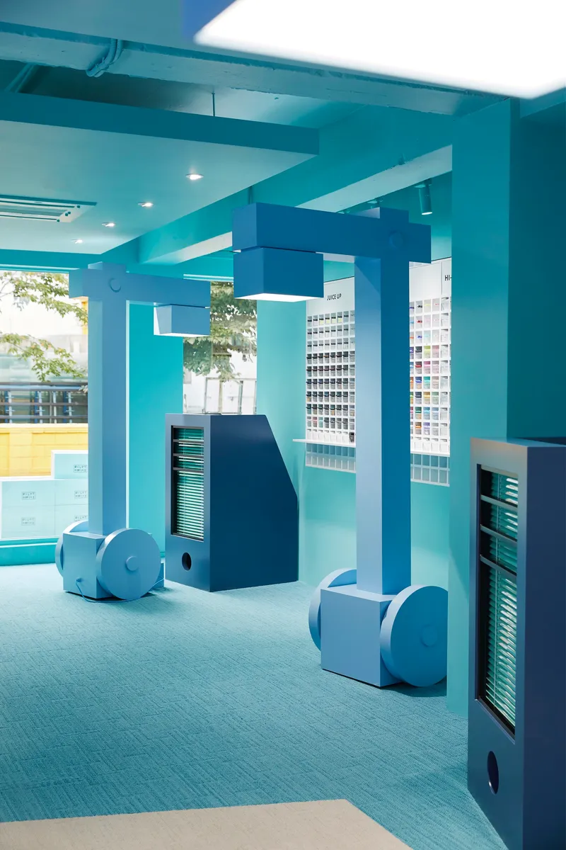 Interior corridor with square columns and curved blue storage forms on the floor near glazed openings
