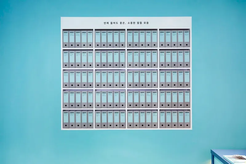 Wall-mounted grid of labeled binder boxes arranged in five rows against a teal surface