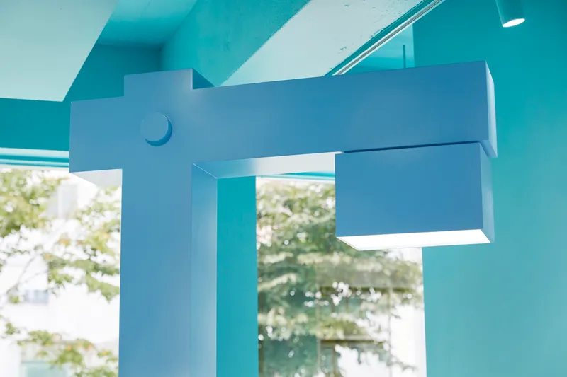 Articulated pale blue display mount with cylindrical joint viewed through glass with trees beyond