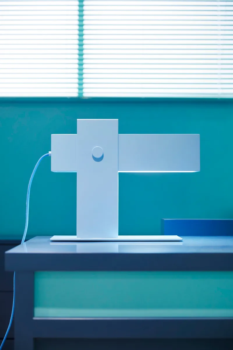 White cross-shaped display stand on a platform with venetian blind shadow above
