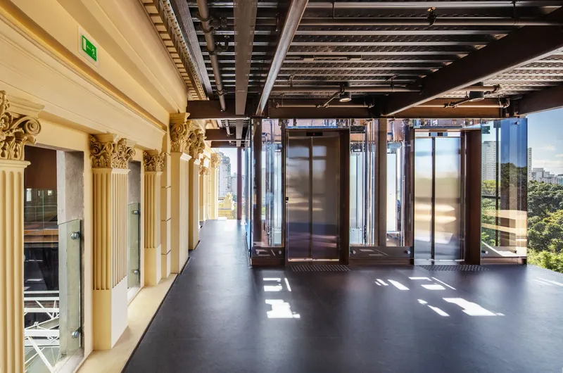 Lobby with ornamental cream columns, exposed ceiling structure, and glass-enclosed elevators with afternoon sunlight