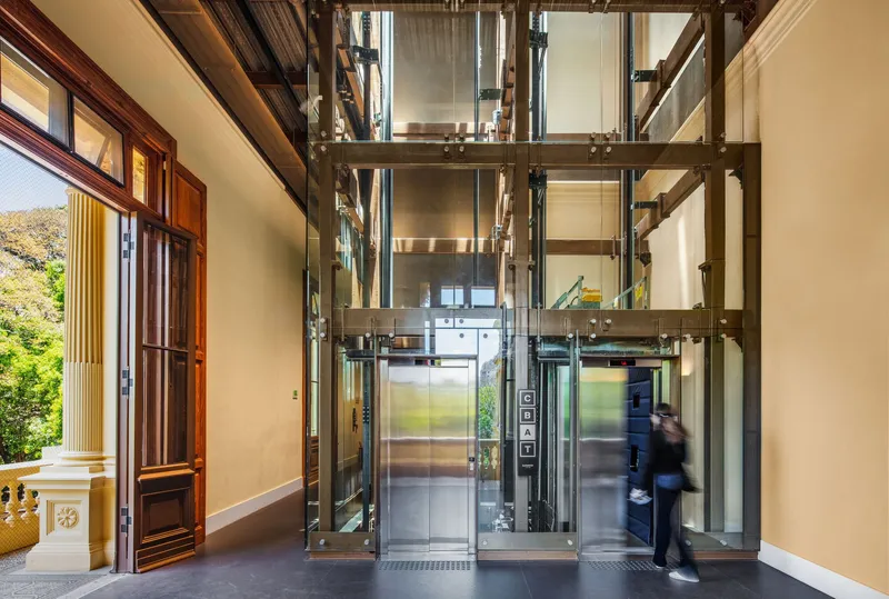 Glass elevator shaft with exposed mechanical systems and a person in motion passing through the lobby