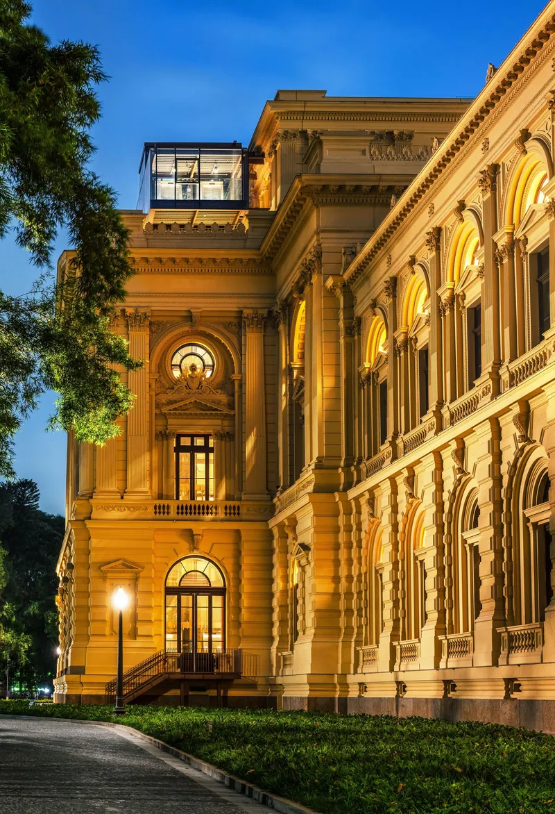 Corner view of ornamental stone facade with arched openings and columns illuminated at dusk