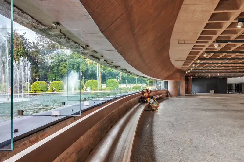 Interior corridor with tiered timber seating along a glass wall overlooking a fountain and gardens