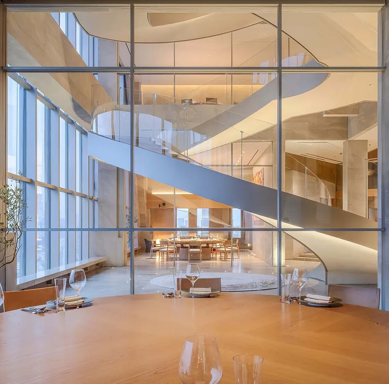 View through steel-framed glass partition of spiraling white staircases connecting multiple dining floors