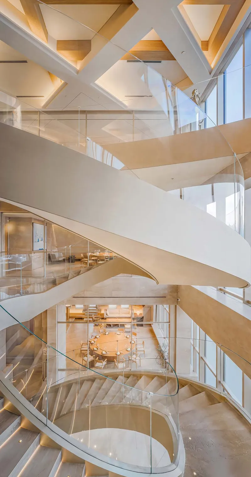 Atrium view of overlapping white ribbon stairs below geometric coffered ceiling with triangular panels