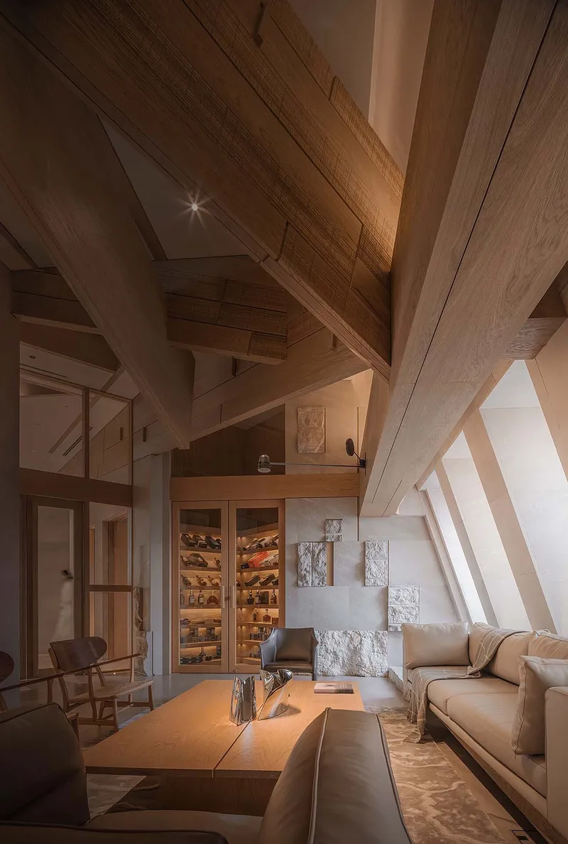 Lounge interior with diagonal timber ceiling beams and built-in illuminated wine display in evening light