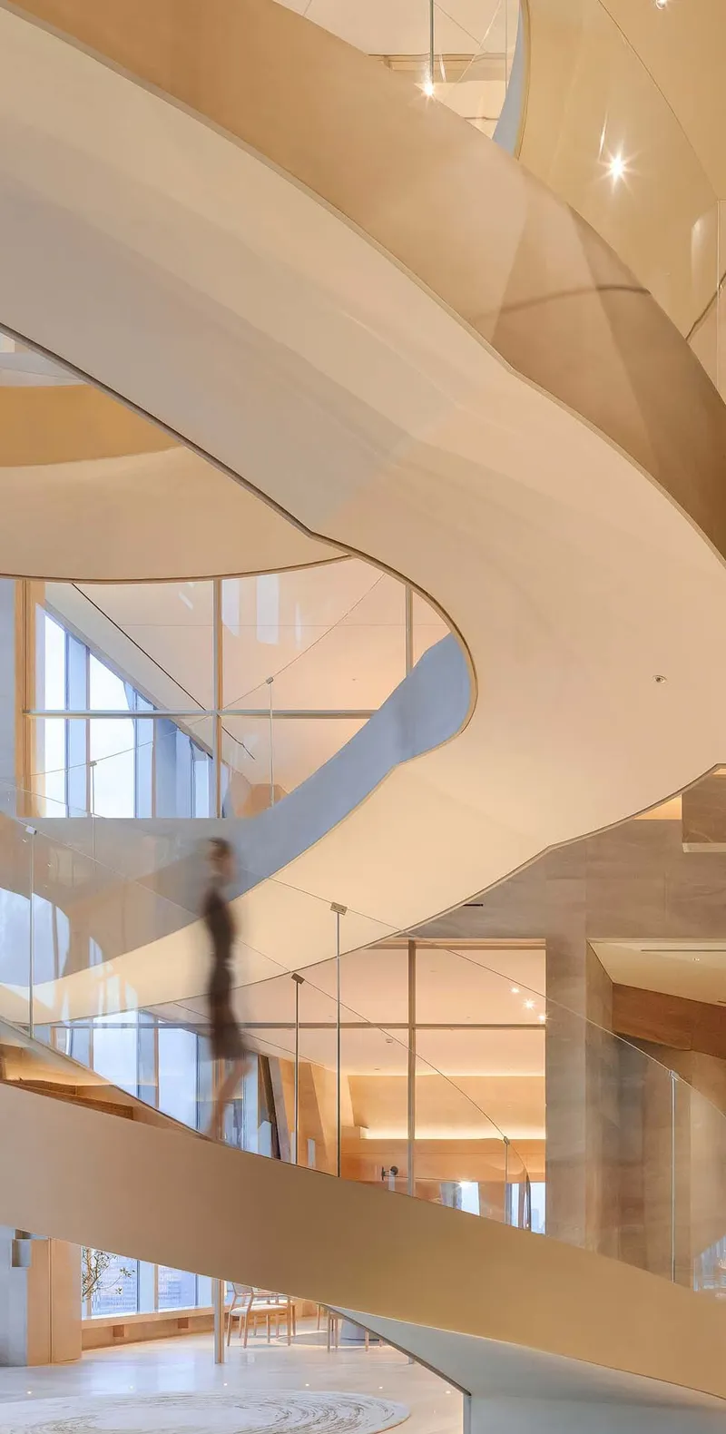 Curved interior staircase with glass railings wrapping through a multi-story atrium with a blurred figure descending