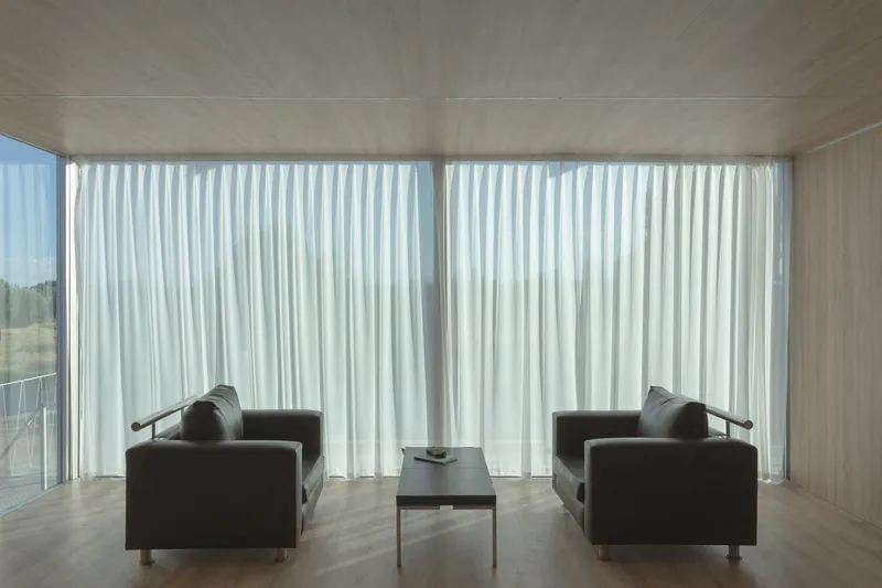 Interior living space with plywood ceiling and floor-to-ceiling white curtains filtering daylight