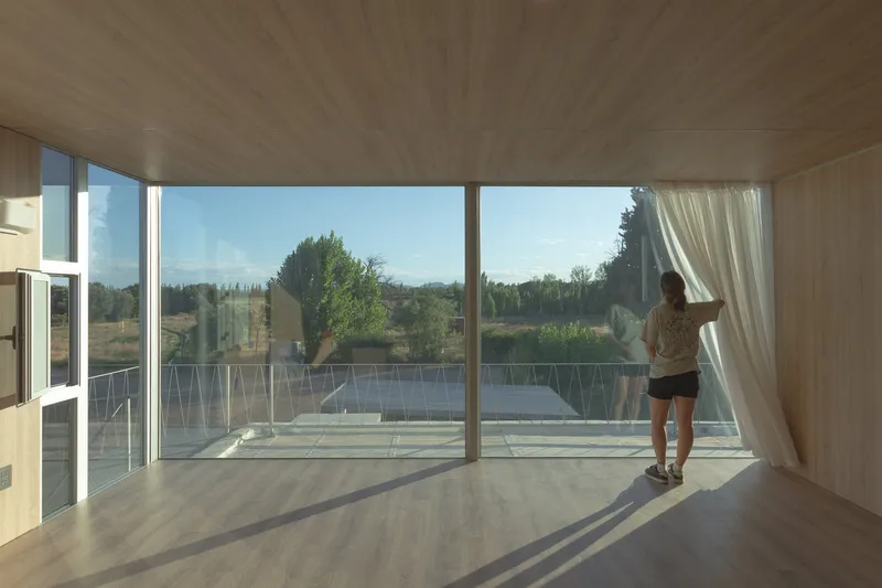 Woman drawing curtain beside full-height glazing overlooking landscape with mountains in distance